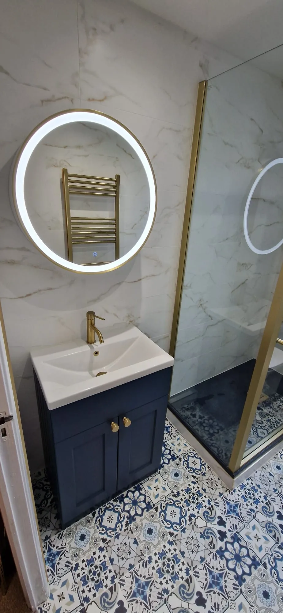 Navy vanity and round mirror beside a brass shower screen